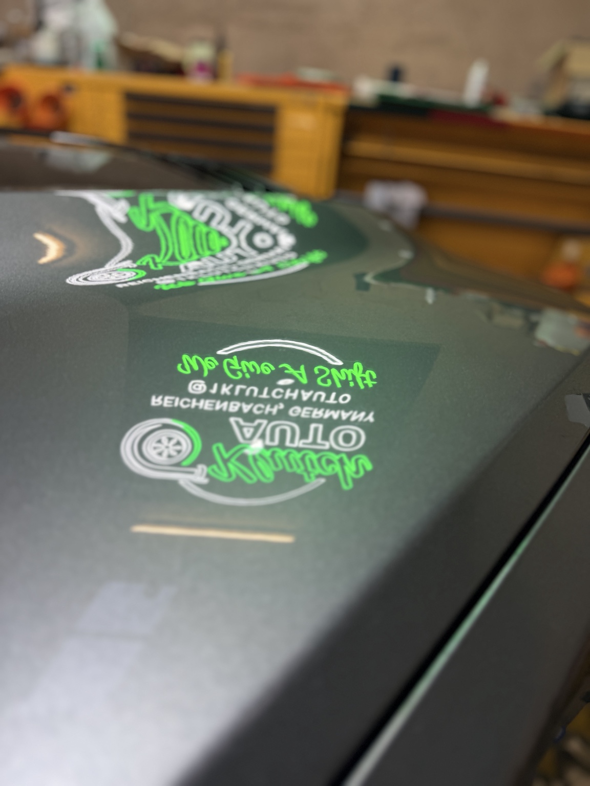 Glossy vehicle hood reflecting green and white workshop signage